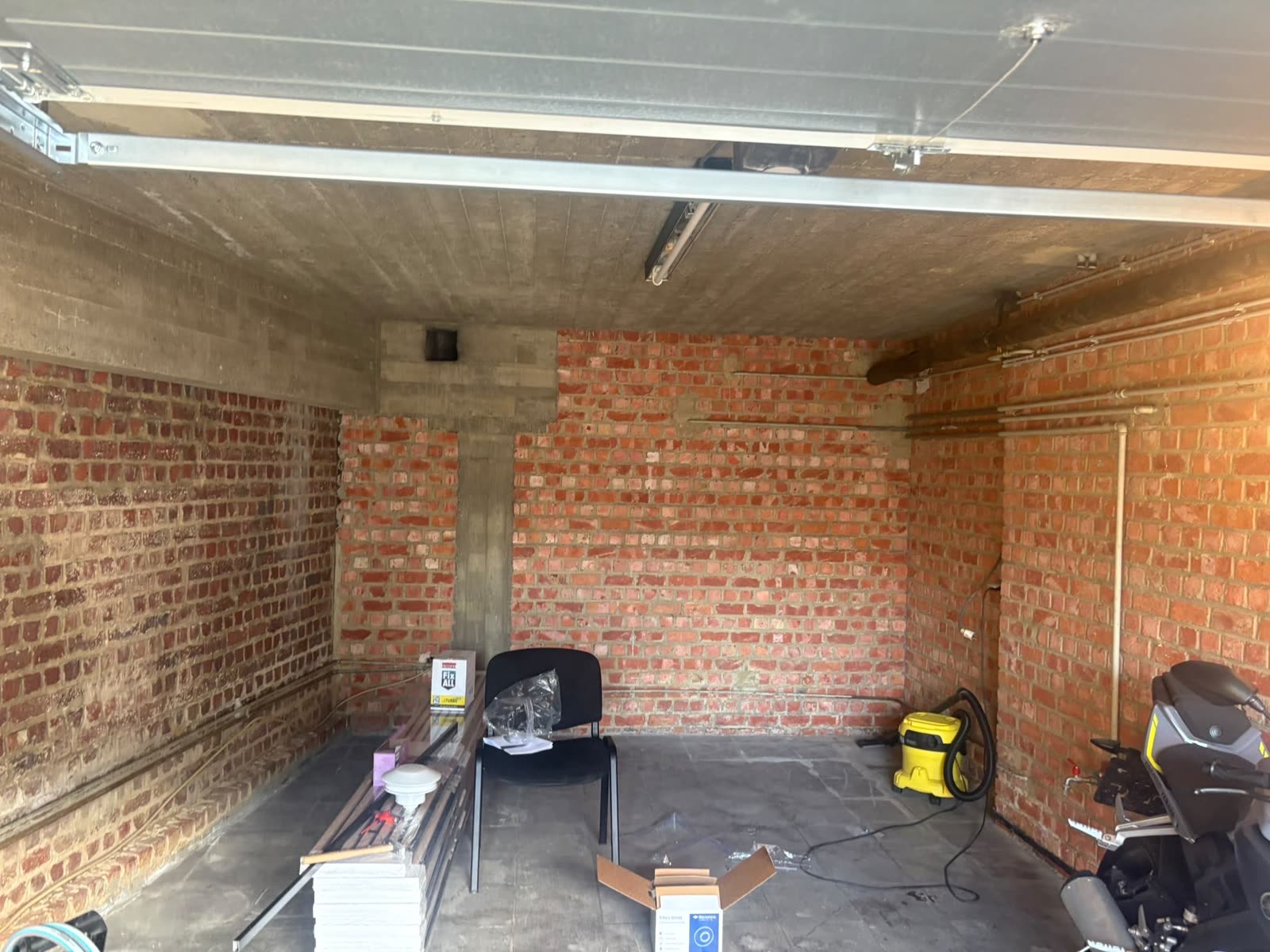 Garage avant les travaux : murs en briques nues, un seul tube au plafond